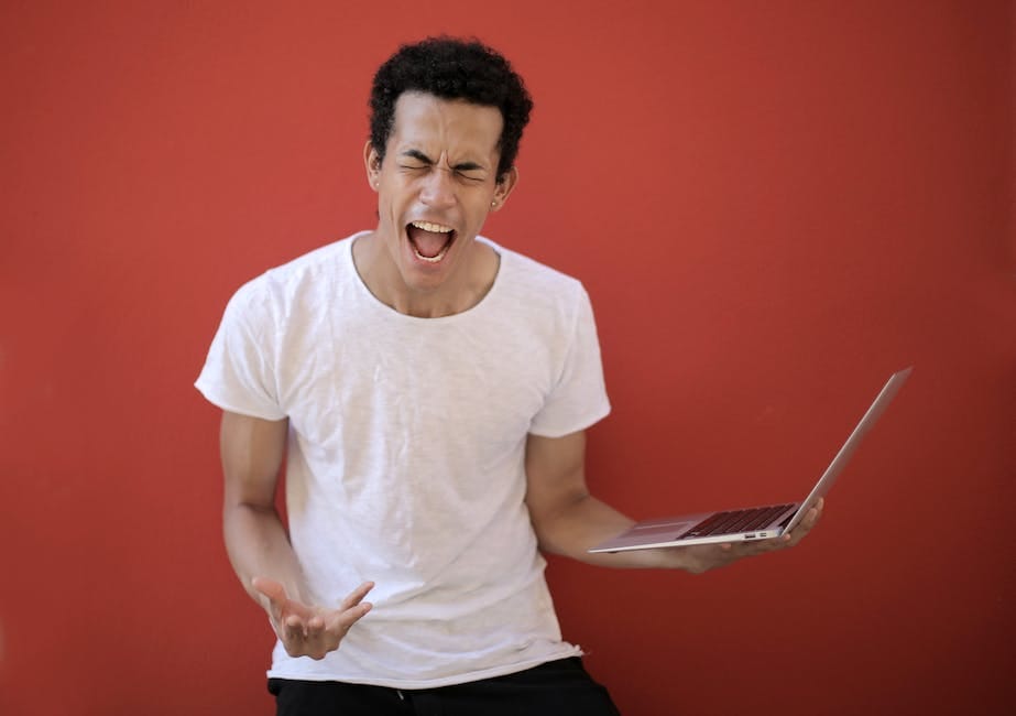 Guy with opened mouth and closed eyes screaming madly while standing with laptop against red background